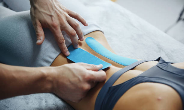 Doctor helps woman by shoulder treatment with kinesio tape.
